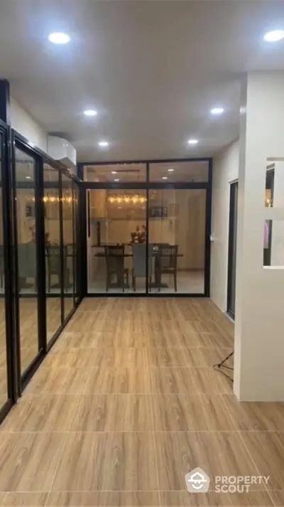 Spacious and elegantly lit living space with modern wood flooring and large glass doors leading to a cozy dining area, perfect for entertaining.