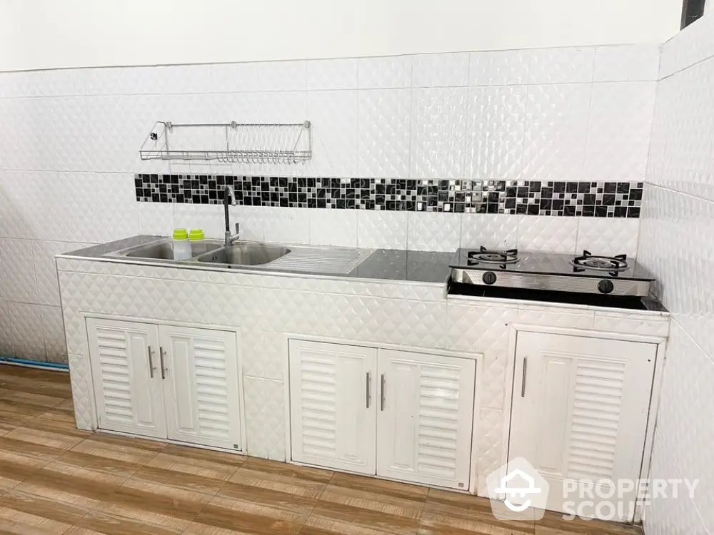 Compact kitchen space with modern gas stove and ample cabinet storage, featuring stylish mosaic backsplash and stainless-steel sink.