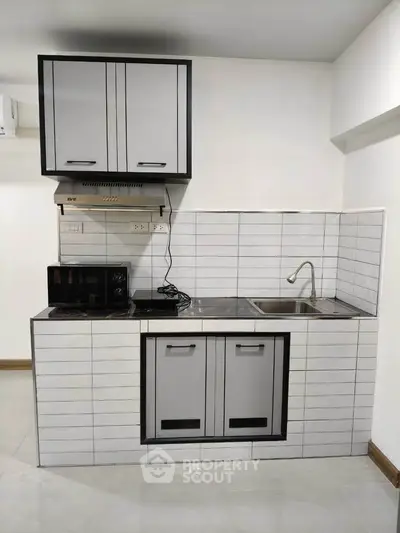 Modern compact kitchen with sleek cabinetry and tiled backsplash, featuring a microwave and sink.