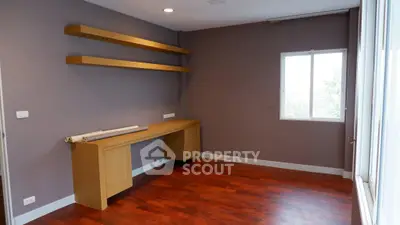 Spacious study room with wooden shelves and desk, featuring large window for natural light.