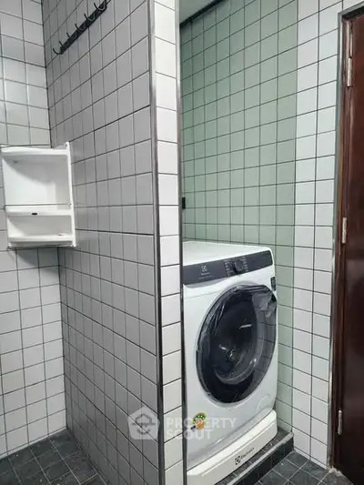 Compact laundry area with modern washing machine in tiled bathroom corner.