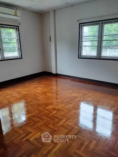 Spacious empty room with polished wooden floors and large windows.