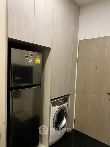 Modern laundry area with washing machine and fridge in sleek cabinetry.