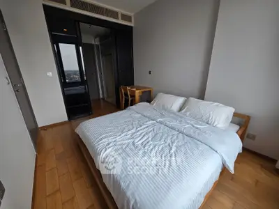 Spacious bedroom with wooden flooring and large window offering city views.