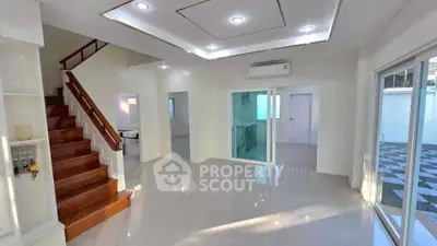 Spacious modern living room with sleek staircase and open kitchen layout, featuring large windows for natural light.