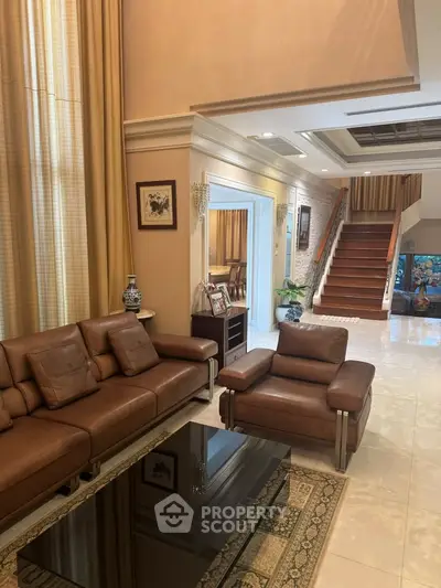 Luxurious living room with elegant leather furniture and staircase in a spacious home.