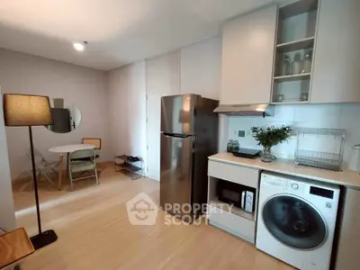 Modern kitchen with stainless steel fridge, washing machine, and dining area in open layout.