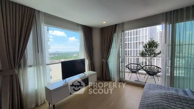 Modern living room with balcony and city view, featuring stylish furniture and large windows.