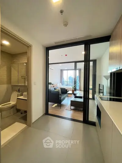 Modern apartment interior with open living room and adjacent bathroom, featuring sleek design and natural light.
