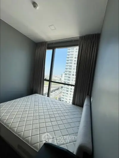 Modern bedroom with large window offering city view, featuring a comfortable mattress and sleek design.