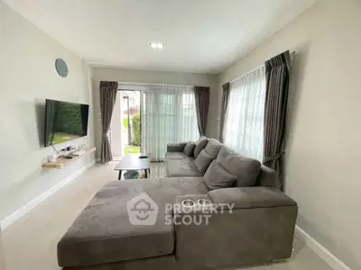 Spacious living room with modern gray sectional sofa and wall-mounted TV, featuring large windows for natural light.