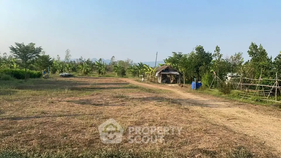 Expansive rural land with lush greenery and a rustic hut, perfect for agricultural development or serene retreat.