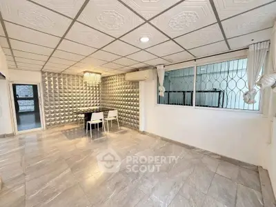 Spacious living room with modern decor and elegant ceiling tiles, featuring a dining area and large windows.