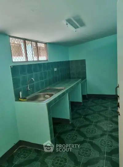 Compact kitchen with teal tiles and single sink, ideal for efficient cooking space.