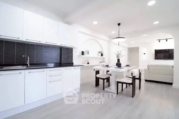 Modern open-plan kitchen and dining area with sleek white cabinetry and stylish decor.