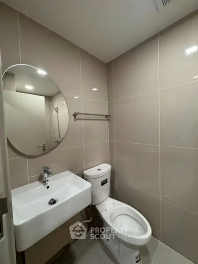Modern bathroom with sleek fixtures and neutral tiles, featuring a round mirror and contemporary design.