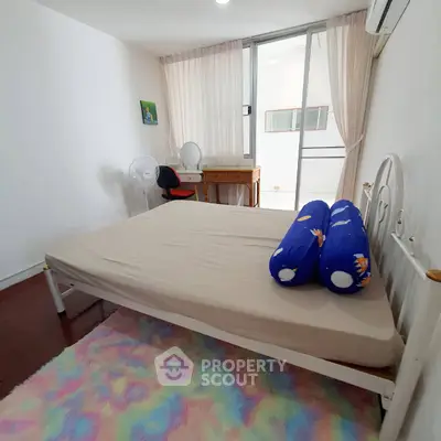 Cozy bedroom with natural light, featuring a desk and colorful rug, ideal for a serene living space.