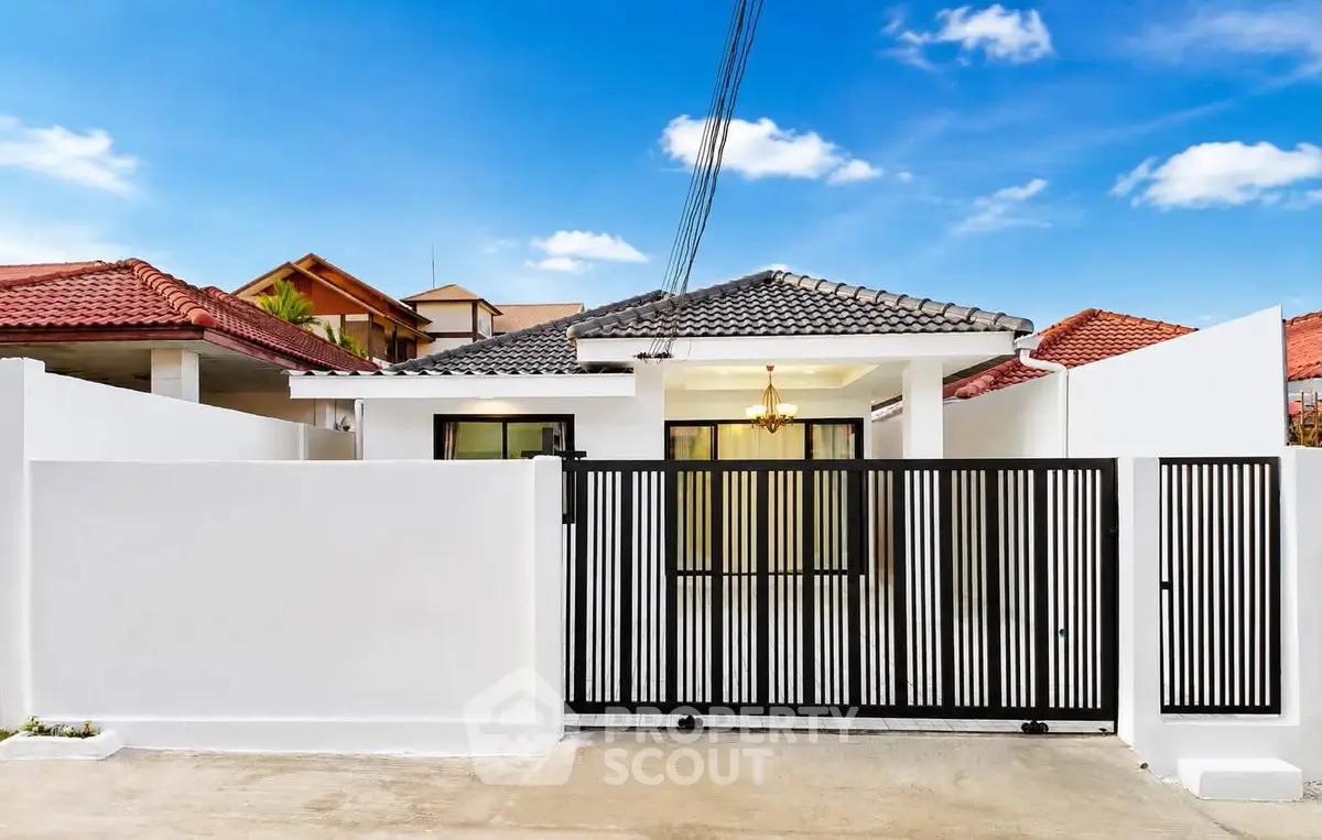Charming single-story home with modern gate and tiled roof under a clear blue sky.