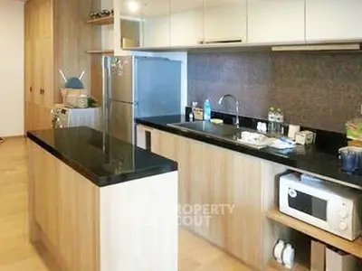 Modern kitchen with sleek wooden cabinetry and black countertops, featuring stainless steel appliances and a microwave.