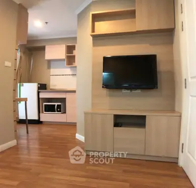 Modern living room with wooden flooring, wall-mounted TV, and compact kitchen area.
