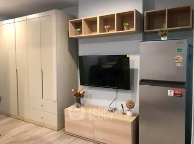 Modern living room with sleek storage, wall-mounted TV, and stainless steel fridge.