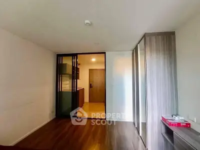 Modern apartment interior with wooden flooring and sliding glass doors leading to kitchen area.