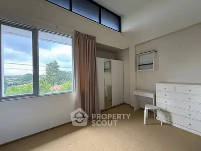 Spacious bedroom with large window and modern furniture, offering a serene view.
