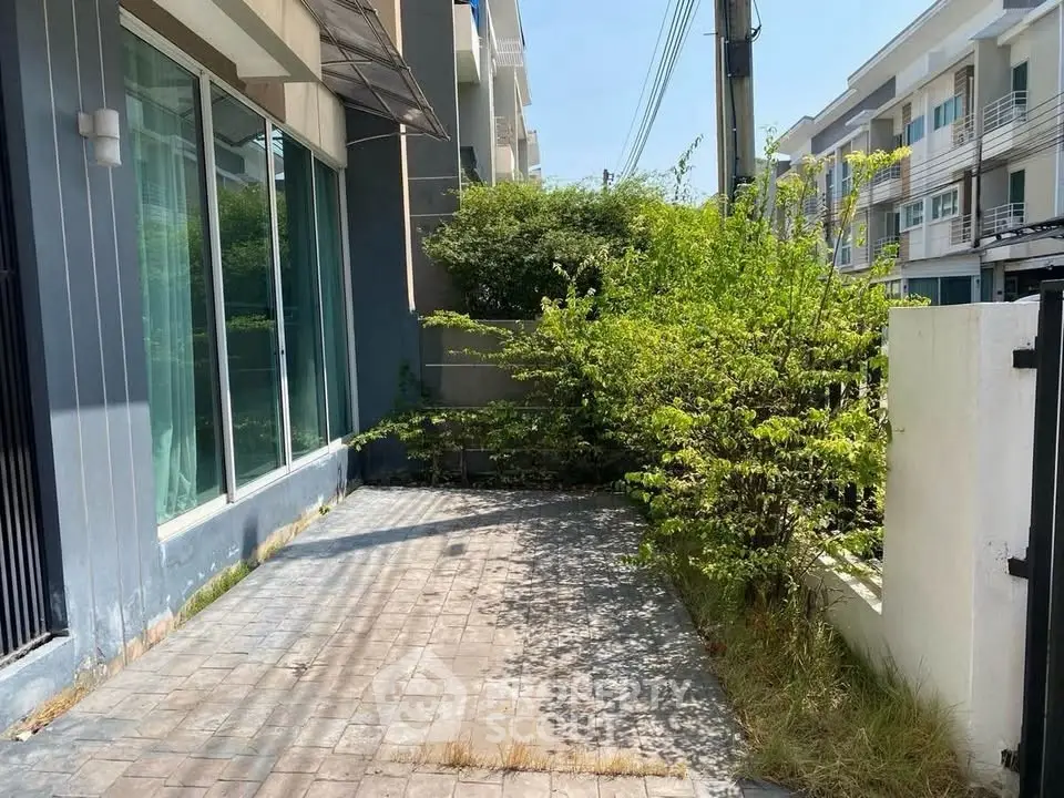 Charming townhouse exterior with lush greenery and paved driveway in a serene neighborhood.