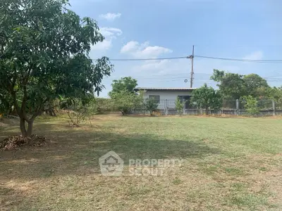 Spacious garden area with lush greenery and a small house in the background.