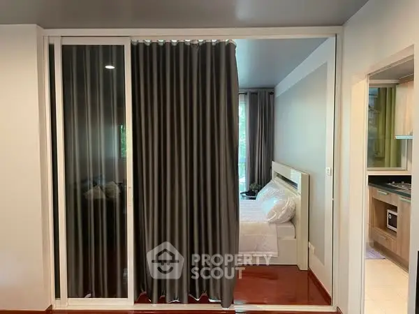 Modern compact bedroom with sliding glass doors and elegant curtains, adjacent to a sleek kitchen area.
