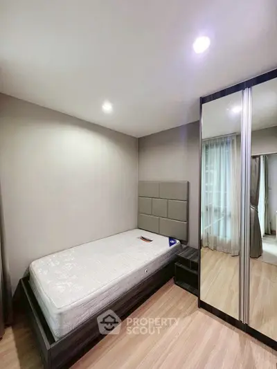 Modern bedroom with sleek design and mirrored wardrobe, featuring a single bed and wooden flooring.