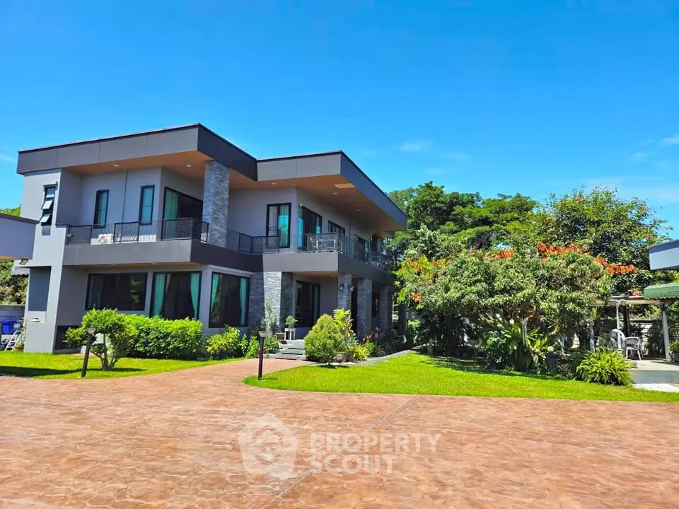 Modern two-story house with lush garden and spacious driveway under clear blue sky.