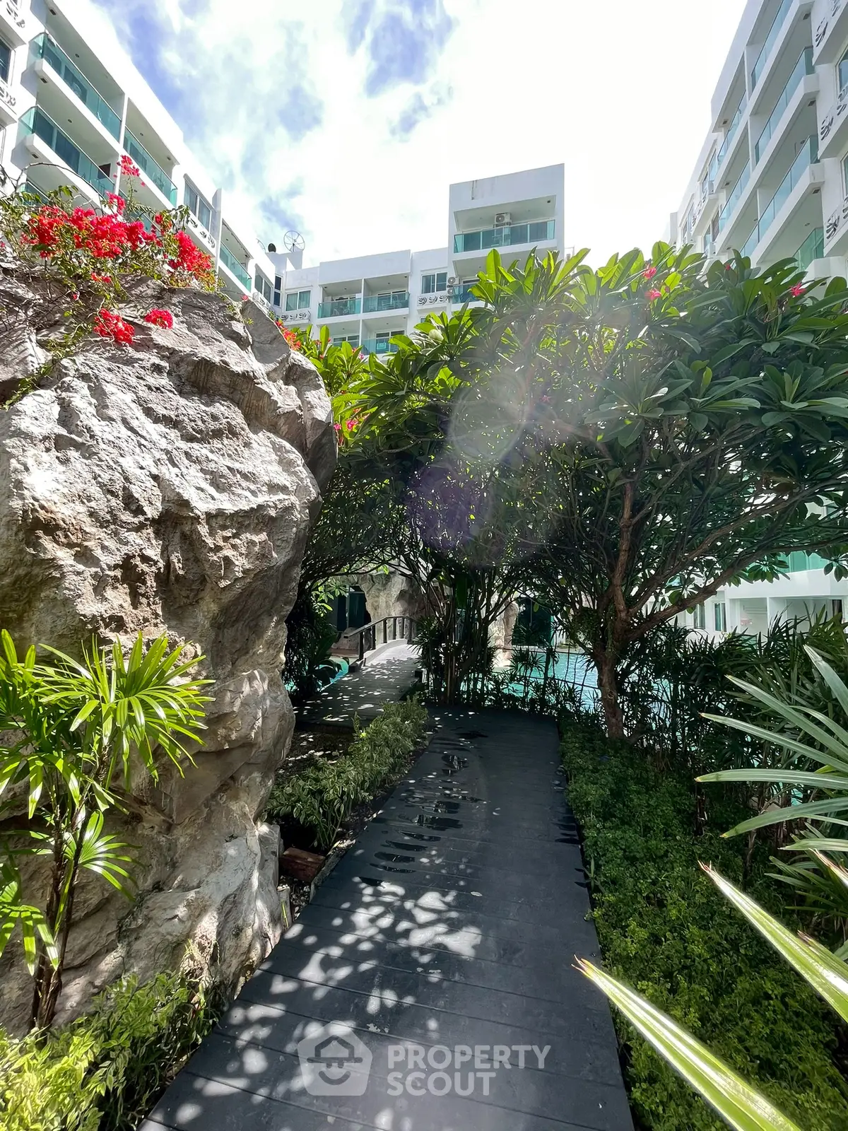 Lush garden pathway leading to a modern apartment complex with vibrant greenery and natural rock features.