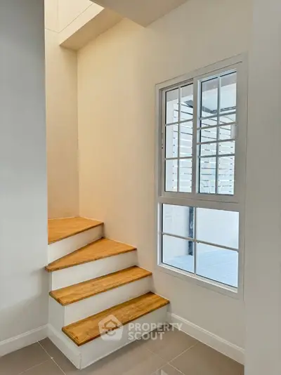 Modern staircase with wooden steps and large window in bright interior