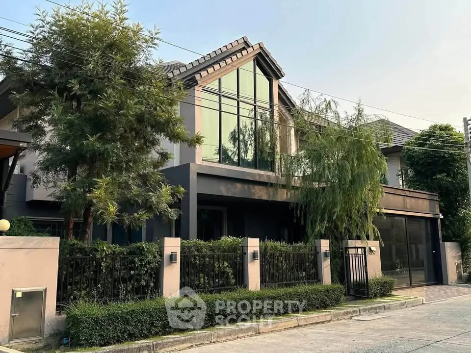 Modern two-story house with large windows and lush greenery in a serene neighborhood.