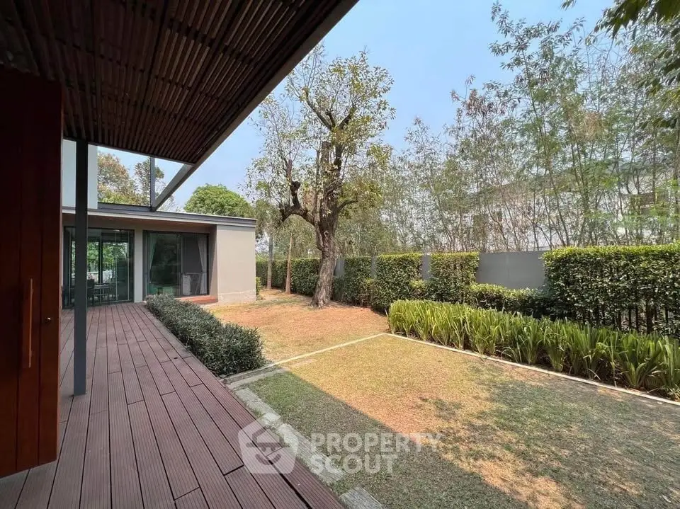 Modern home with spacious garden and wooden deck, surrounded by lush greenery.