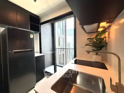 Modern kitchen with sleek black cabinets and stainless steel appliances, featuring a compact balcony view.