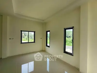 Bright empty room with large windows and tiled floor, offering a serene view of greenery.