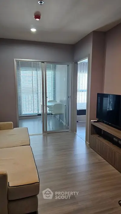 Modern living room with sliding glass doors leading to a bright balcony area, featuring a cozy sofa and flat-screen TV.