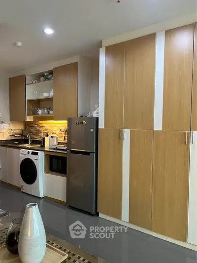 Modern kitchen with sleek cabinets, washing machine, and stainless steel fridge in a stylish apartment.
