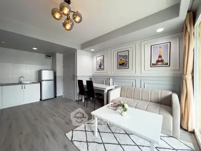 Modern living room with stylish decor and open kitchen layout, featuring elegant lighting and framed artwork.