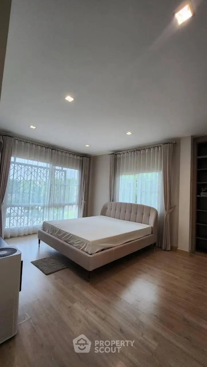 Spacious bedroom with large windows and elegant curtains, featuring a modern bed and wooden flooring.
