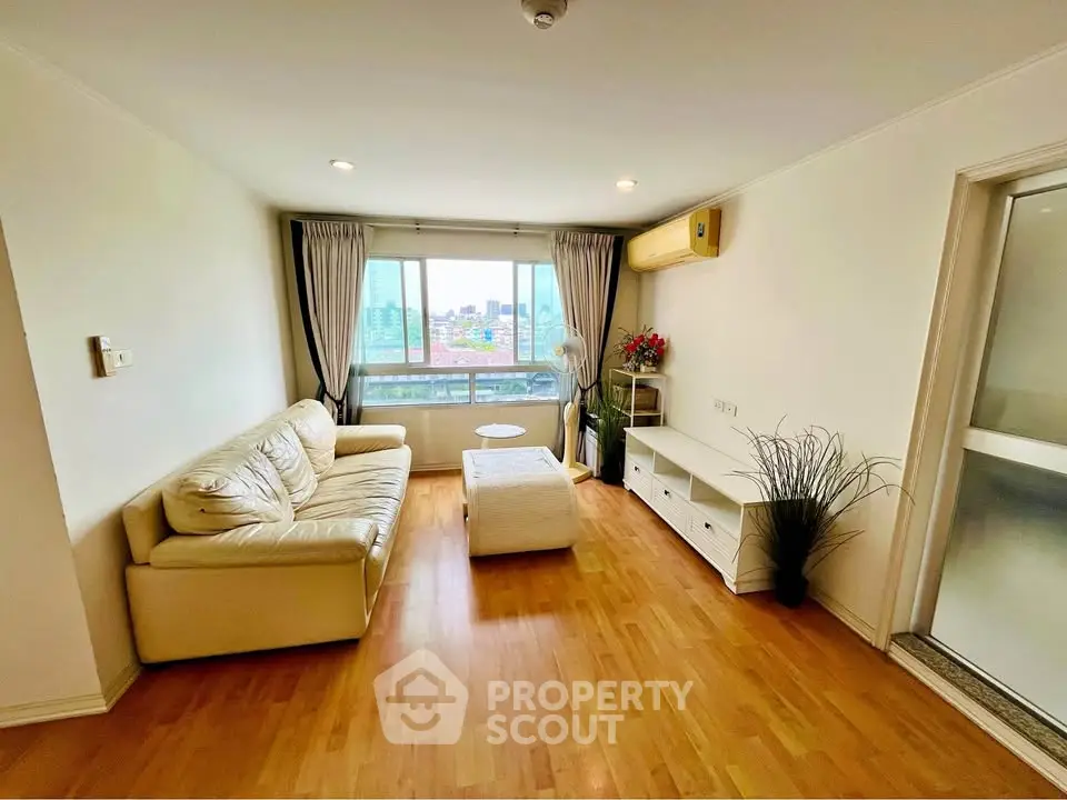Spacious living room with wooden flooring and large window offering city views.