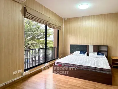 Spacious bedroom with large window and balcony view, featuring modern wooden flooring and elegant decor.