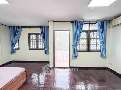 Spacious bedroom with wooden flooring and blue curtains, featuring a balcony access.