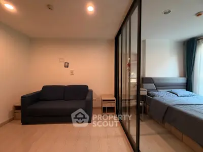Modern studio apartment with cozy living area and comfortable bedroom separated by glass partition.