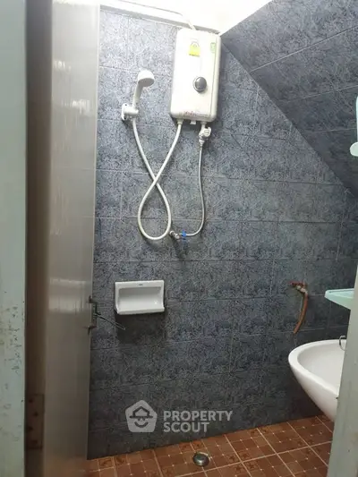 Compact bathroom with shower and tiled walls, featuring a small sink and water heater.