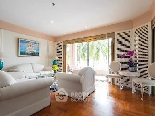 Elegant living room with white furniture and large windows overlooking lush greenery.