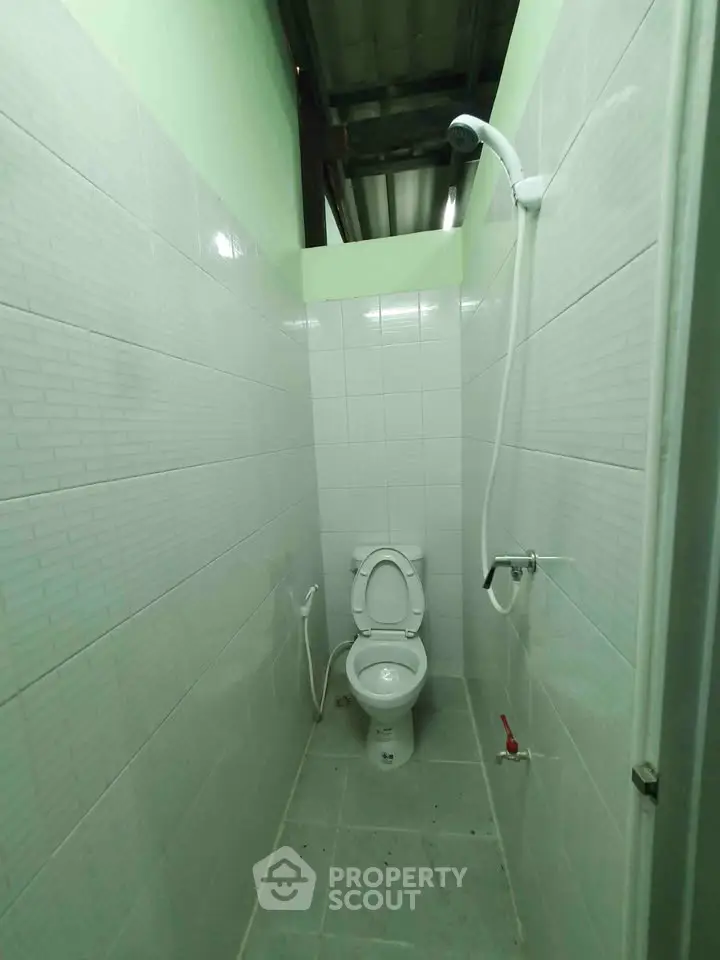 Compact bathroom with tiled walls and showerhead, ideal for efficient space utilization.