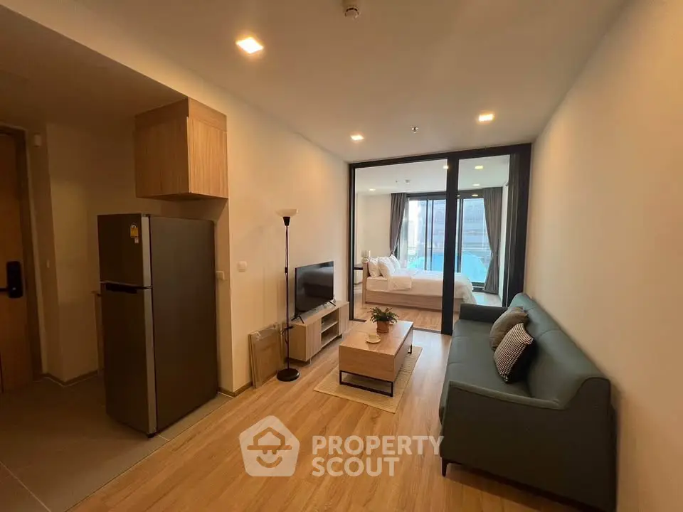 Modern open-plan living room with cozy sofa and TV, leading to a stylish bedroom.